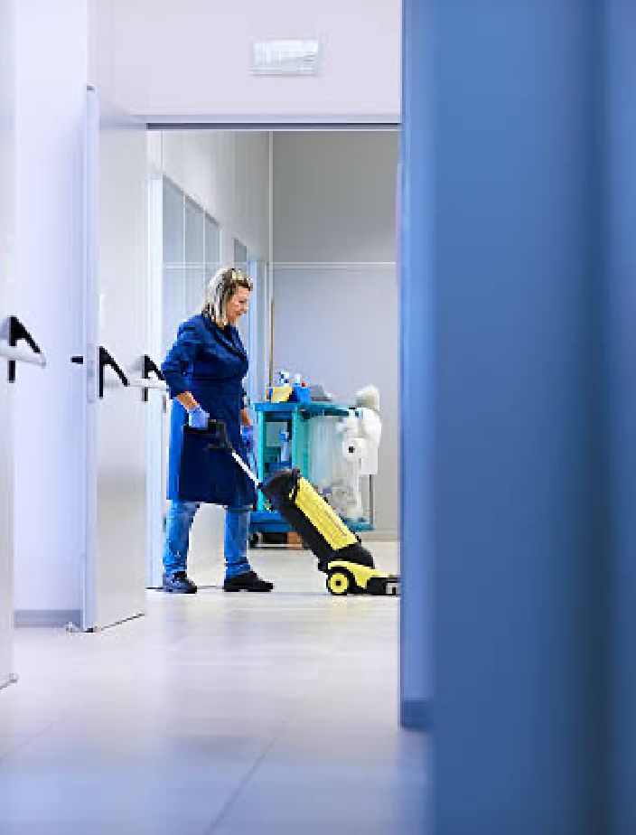 Cleaner vacuuming a hallway in an industrial building.